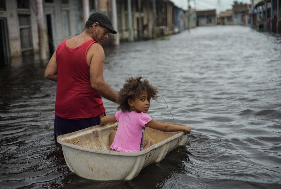Jesus Hernandez guida sua nipote Angelina attraverso un container attraverso una strada allagata a causa dell’uragano Helene, a Batabano, provincia di Mayabeque, Cuba. (AP)