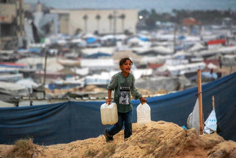 Una ragazza cammina con le taniche per l’acqua vicino alle tende che danno rifugio ai palestinesi sfollati a Khan Yunis, nel sud della Striscia di Gaza. (AFP)