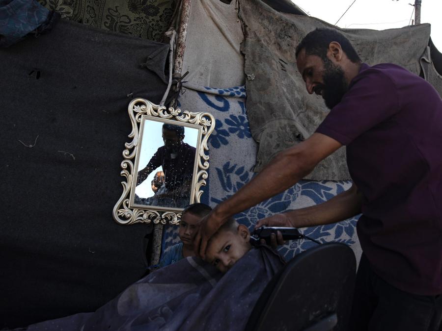 Un barbiere taglia i capelli di un bambino in un campo per sfollati interni palestinesi a Khan Younis, nel sud della Striscia di Gaza. EPA/HAITHAM IMAD