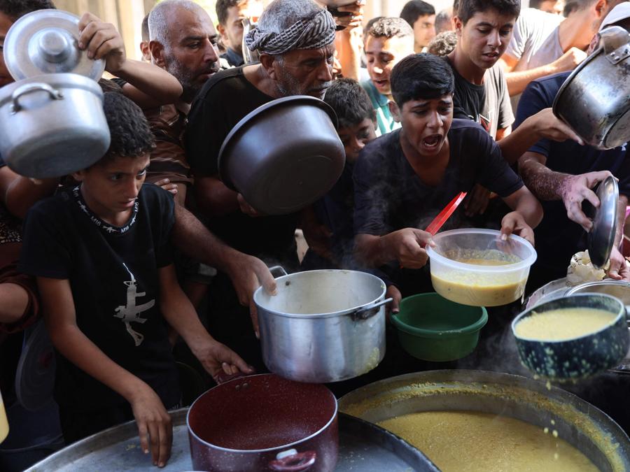 Palestinesi sfollati fanno la fila per ricevere razioni di cibo, offerte da un ente di beneficenza, nel campo profughi di Al-Shati a Gaza. (Photo by Omar AL-QATTAA / AFP)