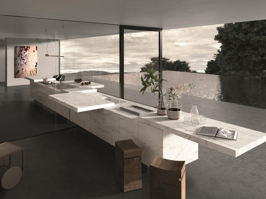 Rossana, K-IN /K-OUT, design Massimo Castagna. Un volume essenziale, un unico blocco esclusivamente a isola in pietra o essenza, disponibile in varie conformazioni, dimensioni e finiture. I piani di lavoro si muovono grazie a meccanismi elettrici concepiti per utilizzo in ambito nautico, i materiali dei piani e delle ante, oltre che la ferramenta, sono stati selezionati in base alla loro resistenza e idoneità all'esposizione esterna. I grandi top coperchio scorrevoli celano le zone di lavoro della cucina, aprendosi in entrambi i sensi e trasformando il blocco monolitico della cucina chiusa in forma e proporzioni. Il movimento funzionante elettricamente grazie ad un sistema a basso voltaggio, permette di nascondere il top interno in cui sono installate cotture e cappe da piano nella versione indoor e i barbecue in quella outdoor. Le due cucine pur essendo visivamente uguali, sono costruite in modo profondamente diverso in virtù delle performance necessarie alla diversa collocazione: strutture in legno nella versione da interno, alluminio per la struttura da esterno.