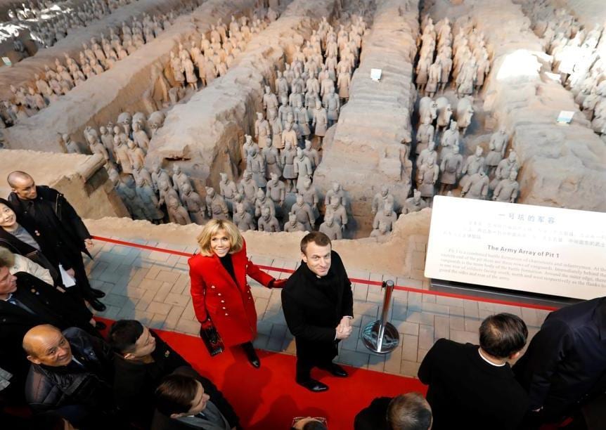 Brigitte ed Emmanuel Macron visitano il celebre sito di Xian dove è conservato l'esercito di terracotta. La premiere dame indossa un cappotto rosso di Balmain abbinato a stivali e borsa Christian Louboutin, con sciarpa nera Louis Vuitton
