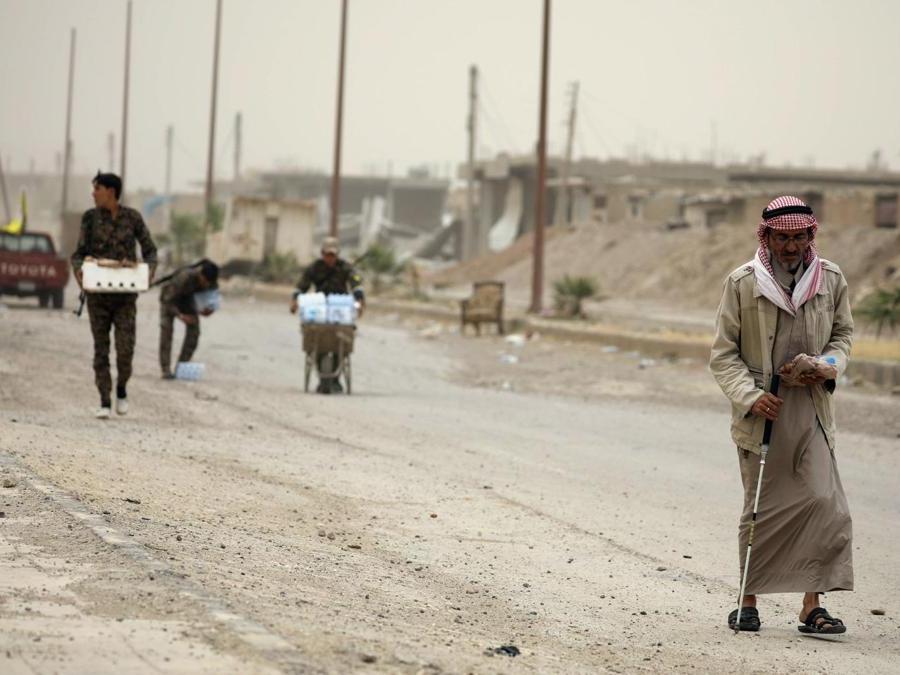 Un civile  e i  combattenti delle forze democratiche siriane (SDF) camminano sulle macerie di una strada danneggiata nel quartiere industriale al-Sanaa di Raqqa. (REUTERS/Rodi Said)