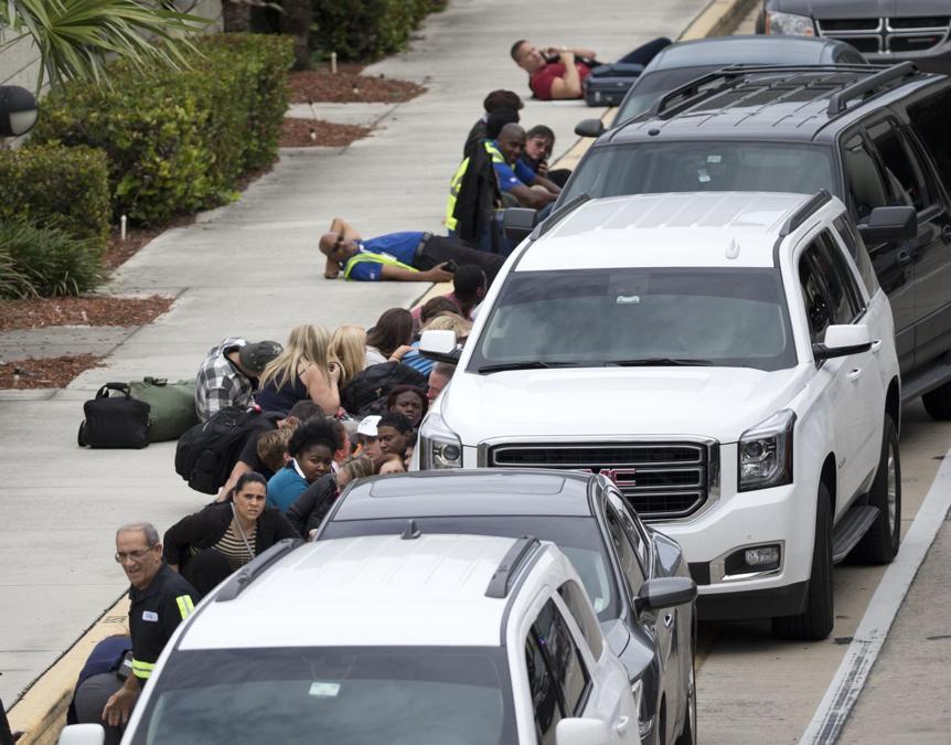 Persone che si riparano dietro le automobili all’esterno dell’aeroporto. (AP Photo/Wilfredo Lee)