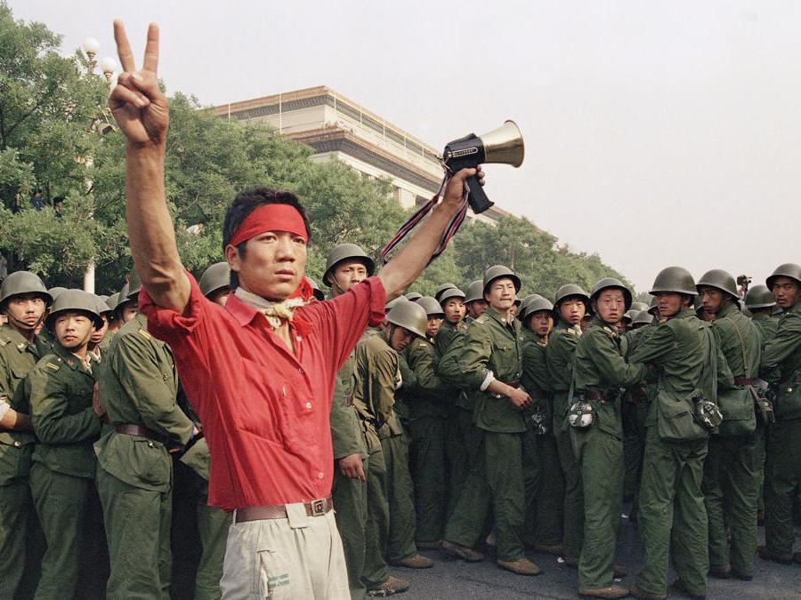 In questa foto del 3 giugno 1989 uno studente manifestante pro-democrazia lancia segnali di vittoria alla folla mentre le truppe dell'Esercito Popolare di Liberazione si ritirano sul lato ovest della Grande Sala del Popolo vicino a Piazza Tiananmen a Pechino.(AP Photo/Mark Avery, File)
