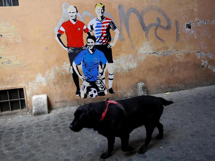 Un cane cammina davanti a un murales firmato da “TV Boy” e raffigurante il presidente russo Vladimir Putin, il presidente degli Stati Uniti Donald Trump e il primo ministro italiano Giuseppe Conte come calciatori nel centro di Roma. REUTERS/Tony Gentile