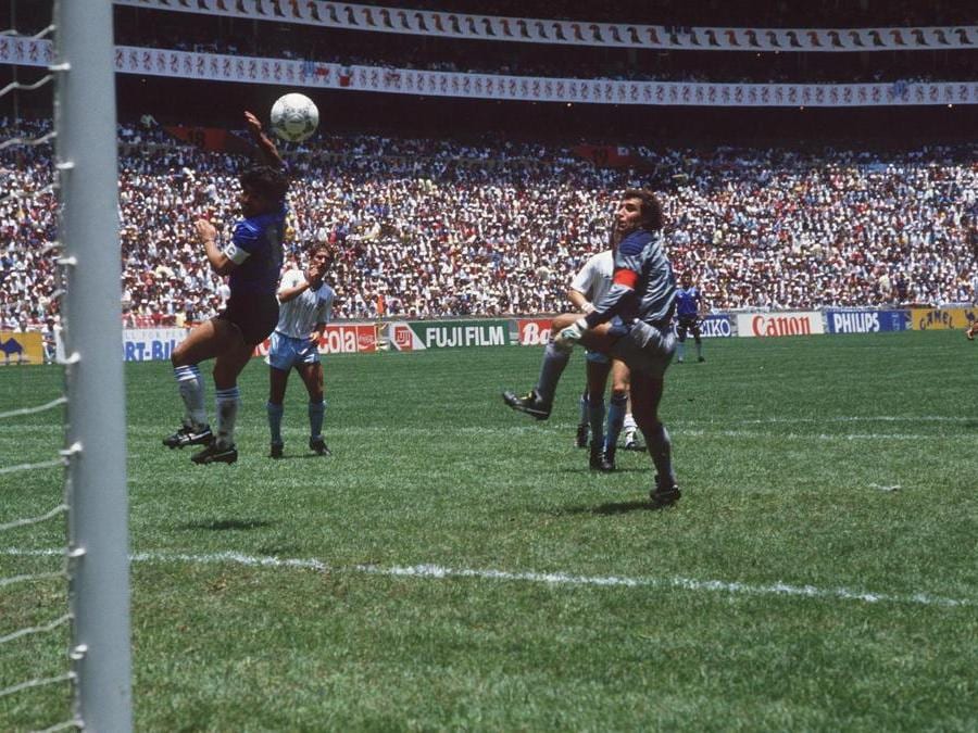 1986. MESSICO. Nel quarto di finale contro l'Inghilterra, Maradona realizza la rete del vantaggio argentino, deviando il pallone in rete con il braccio. L'arbitro tunisino Ali Bin Nasser non si accorge di nulla e convalida la rete. In conferenza stampa, il fuoriclasse argentino, dichiarò che «il  gol è stato regolarissimo, ho colpito la palla di testa, semmai c'è stata mano de Dios». (Afp)