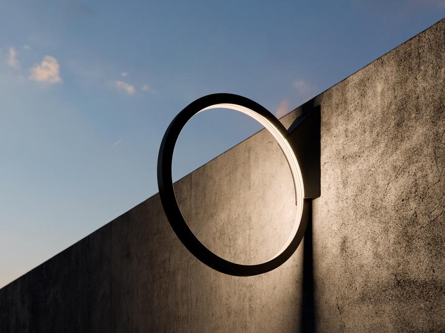 Artemide, O, design Elemental, Alejandro Aravena, Gonzalo Arteaga, Juan Cerda, Victor Oddó, Diego Torres. Nelle versioni outdoor da terra e sospensione oggi proposta anche per gli interni grazie ad una soluzione con cavo che ne consente un semplice riposizionamento. Anche in questo caso il grado di protezione IP resta comunque adatto ad un utilizzo in esterni. La sua leggerezza non è solo formale, il sottile profilo in alluminio diventa quindi a tutti gli effetti un elemento che può essere spostato dove necessario, capace di creare in ogni spazio un'atmosfera piacevole con la sua luce morbida e non abbagliante. Oltre all'originale versione con diametro 90cm “O” si sviluppa in una dimensione più piccola da 45cm (nella foto) che mantiene però tutte le caratteristiche della precedente.Tutte le versioni vengono presentate anche con finitura bianca oltre che nera