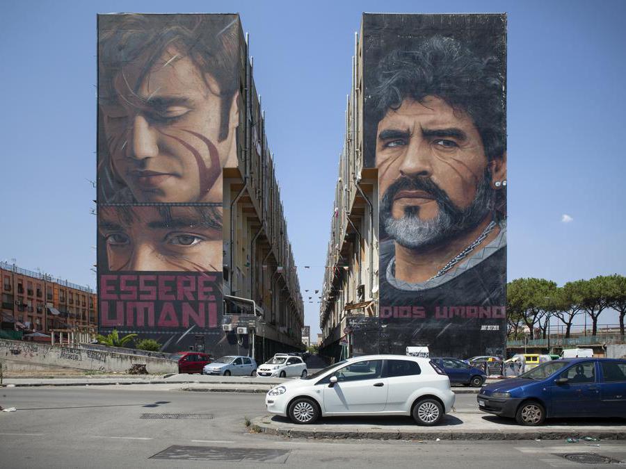 Una veduta dei murales giganti realizzati nel 2018 dallo street artist napoletano Jorit sui palazzi del quartiere San Giovanni, soprannominato «Bronx». Maradona «Dios umano» è ritratto nella sua maturità in modo iperrealista, nello stile inconfondibile del giovane artista. Sulle due facciate diametralmente opposte delle enormi costruzioni popolari, lo stesso autore ha realizzato il più grande ritratto al mondo di Ernesto «Che» Guevara. Il progetto di arte sociale di Jorit e del Comune di Napoli prevede la realizzazione di opere dal forte contenuto simbolico in alcuni dei quartieri più difficili e svantaggiati della città, cercando attraverso la street art di favorirne l’inclusione all’interno del tessuto turistico cittadino. Napoli, agosto 2020. © Paolo Vezzoli