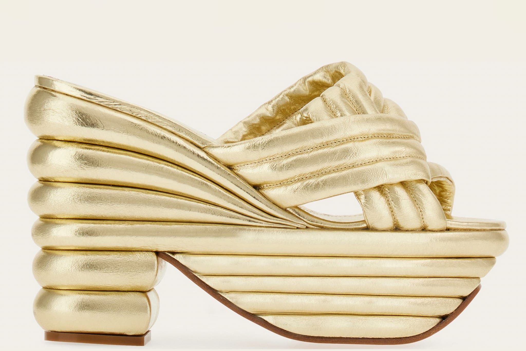 Ferragamo. Sandalo con plateau scultura in nappa laminata con fasce che si intrecciano lateralmente con un nodo ispirato all’origami, mentre le bombature ricordano l’iconico sandalo Rainbow della maison (1.590 €).