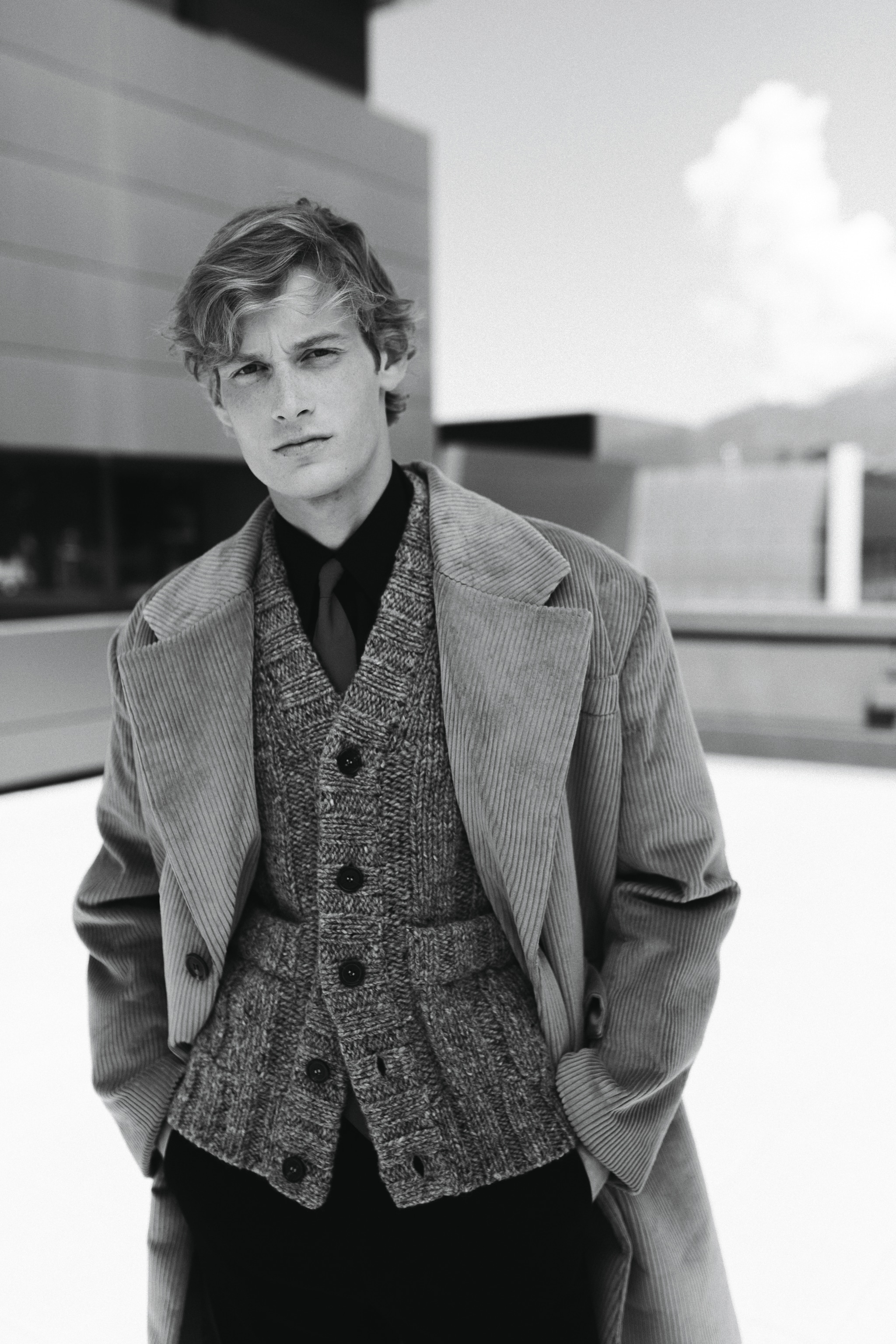 Cappotto oversize in velluto a coste, cardigan gilet in lana con tasche applicate, cravatta in seta e camicia in cotone, pantaloni in fresco lana, Prada. 