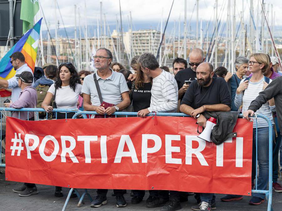 People holding a banner reading "open harbours" demonstrate in protest to let disembark 35 remaining migrants from the rescue ship "Humanity 1" of German organisation SOS Humanity, which carries 179 rescued migrants, on November 6, 2022 after it arrived at the port of Catania, Sicily. - 144 rescued migrants out of 179 have been allowed to disembark to be medically examined in Catania from "Humanity 1", which has been waiting for a safe harbour for two weeks. Italy readied on November 6 to allow vulnerable migrants off the charity rescue vessel in Sicily, but sources close to firebrand minister Matteo Salvini warned those not eligible to remain would be forced back into international waters. (Photo by Giovanni ISOLINO / AFP)