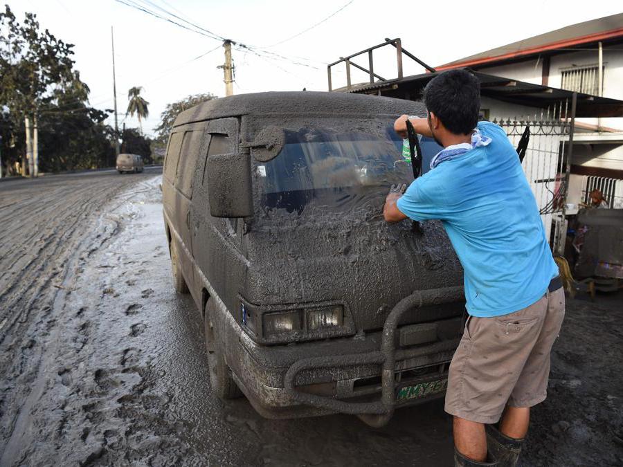 Un residente pulisce fango e cenere dalla sua auto dopo che il vulcano Taal ha iniziato a eruttare cenere sulla città di Tanauan, provincia di Batangas a sud di Manila. (Photo by Ted ALJIBE / AFP)