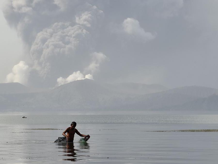 Un pescatore guada con le sue reti nelle acque del lago Taal mentre il vulcano Taal emette cenere visto dalla città di Tanauan nella provincia di Batangas, a sud di Manila. (Photo by Ted ALJIBE / AFP)