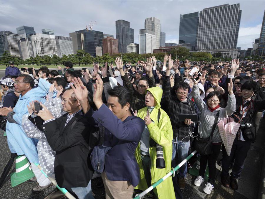 Le persone al di fuori del Palazzo Imperiale di Tokyo seguono i tre “banzai” del Primo Ministro Shinzo Abe . (AP Photo/Eugene Hoshiko)