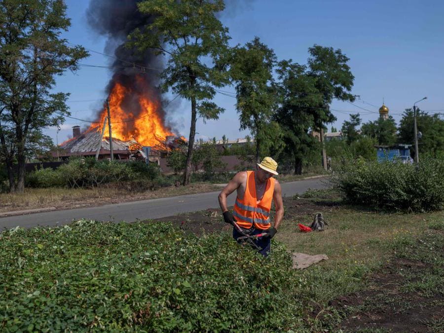 Un operaio municipale taglia gli alberi sui marciapiedi davanti a una casa in fiamme colpita da una granata nella periferia di Bakhmut, nell’Ucraina orientale (Bulent Kilic/Afp) 