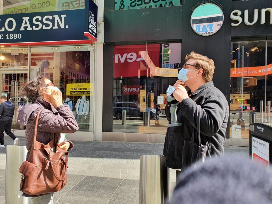Una signora sinoamericana regala una mascherina a uno studente italiano sui marciapiedi vicino a Times Square: Stay safe.