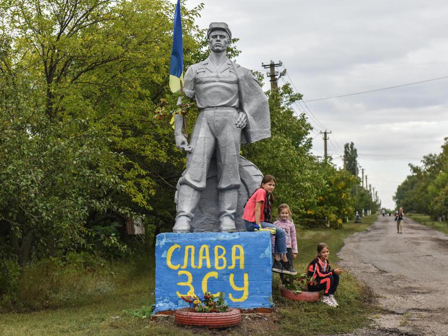 Bambini siedono su un monumento, dipinto con le parole “Gloria all’AFU” (Forze armate dell’Ucraina) nella regione di Kharkiv. (Epa/ Oleg  Petrasyuk)
