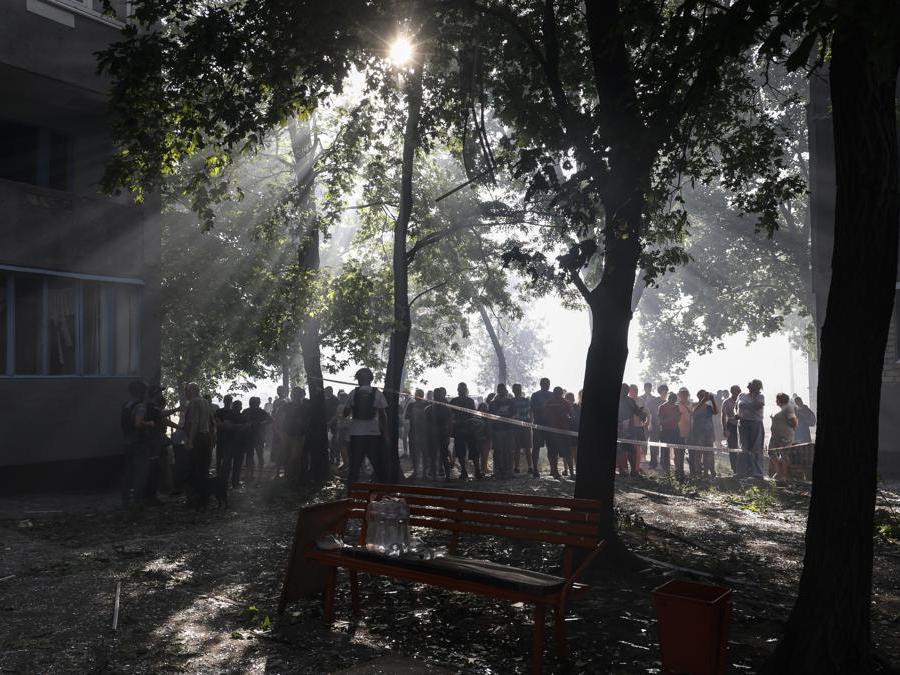 La gente del posto si trova dietro un cordone vicino al sito di un edificio residenziale di 12 piani danneggiato a seguito di un attacco missilistico a Kharkiv, nel nord-est dell’Ucraina. EPA/SERGEY KOZLOV
