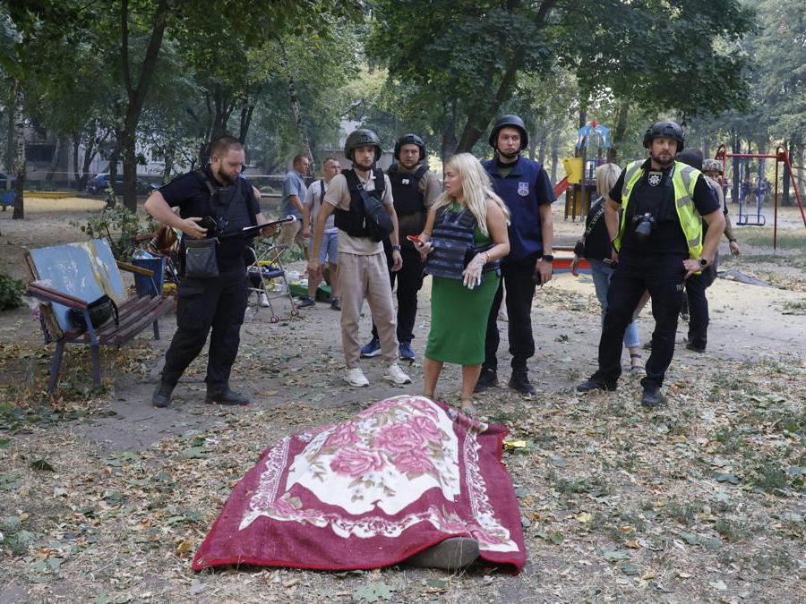 Agenti di polizia ucraini si trovano vicino ai corpi coperti delle vittime vicino al sito di un edificio residenziale di 12 piani danneggiato a seguito di un attacco missilistico a Kharkiv, nel nord-est dell’Ucraina. EPA/SERGEY KOZLOV