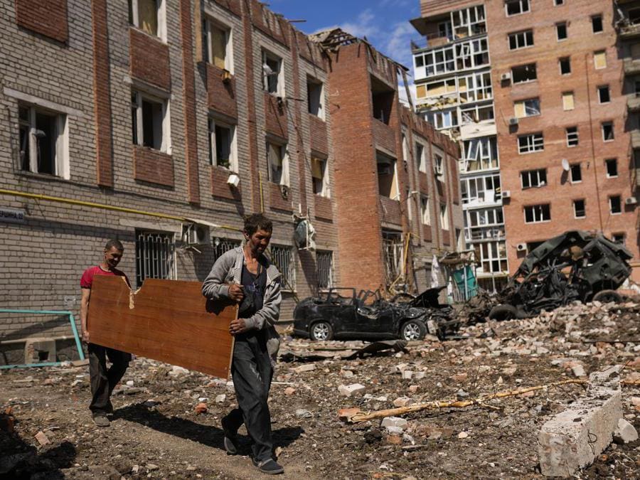 Due uomini trasportano un pannello di legno accanto a edifici gravemente danneggiati e auto distrutte in un bombardamento russo a Bakhmut, nell’Ucraina orientale (AP Photo/Francisco Seco)